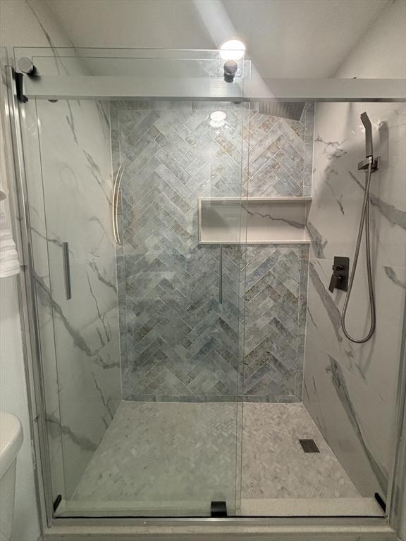 bathroom featuring toilet and a marble finish shower