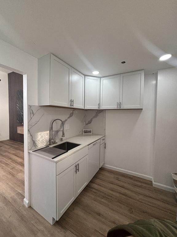 kitchen featuring a sink, wood finished floors, white cabinetry, light countertops, and dishwasher