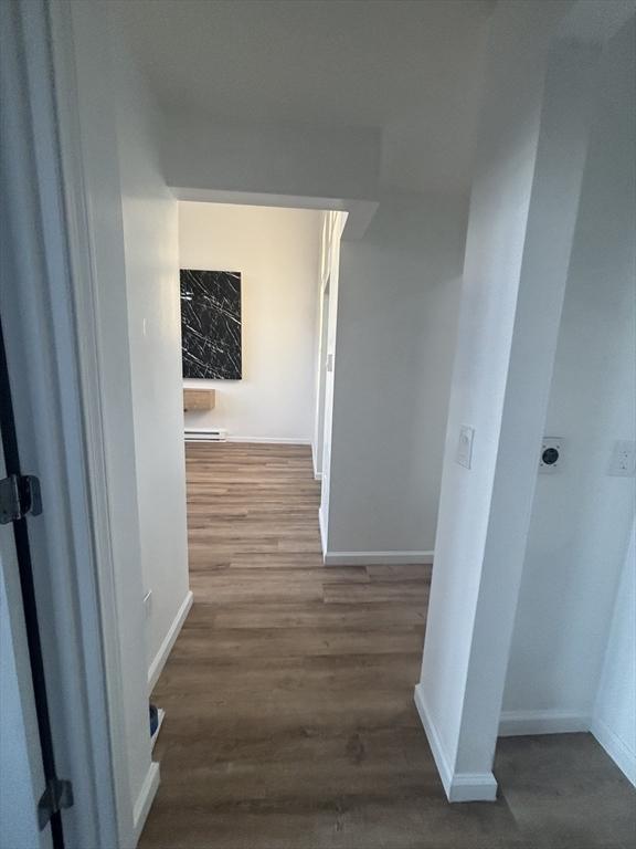 hallway with baseboard heating, wood finished floors, and baseboards