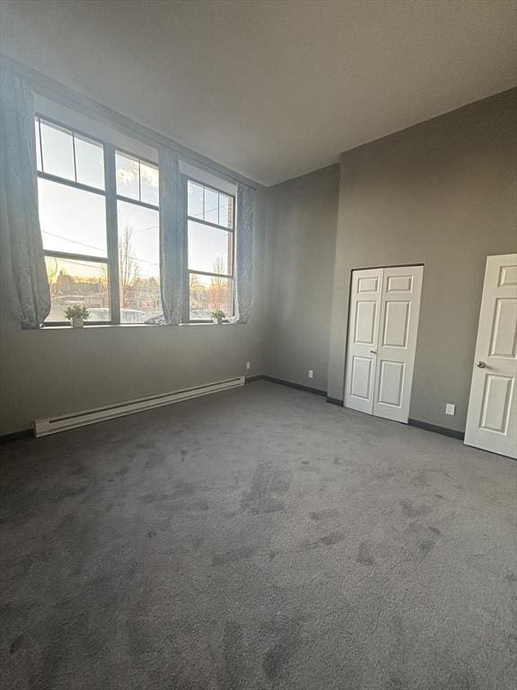 carpeted spare room with a baseboard heating unit, baseboards, and a healthy amount of sunlight