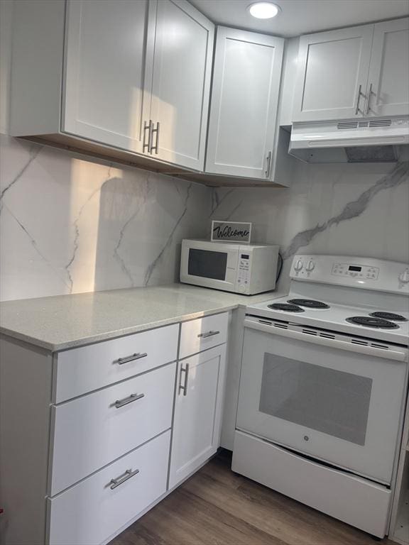 kitchen featuring white appliances, under cabinet range hood, white cabinetry, and dark wood-type flooring