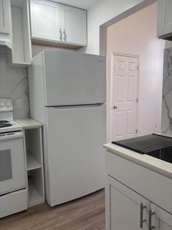 kitchen with decorative backsplash, white appliances, white cabinets, and light wood finished floors