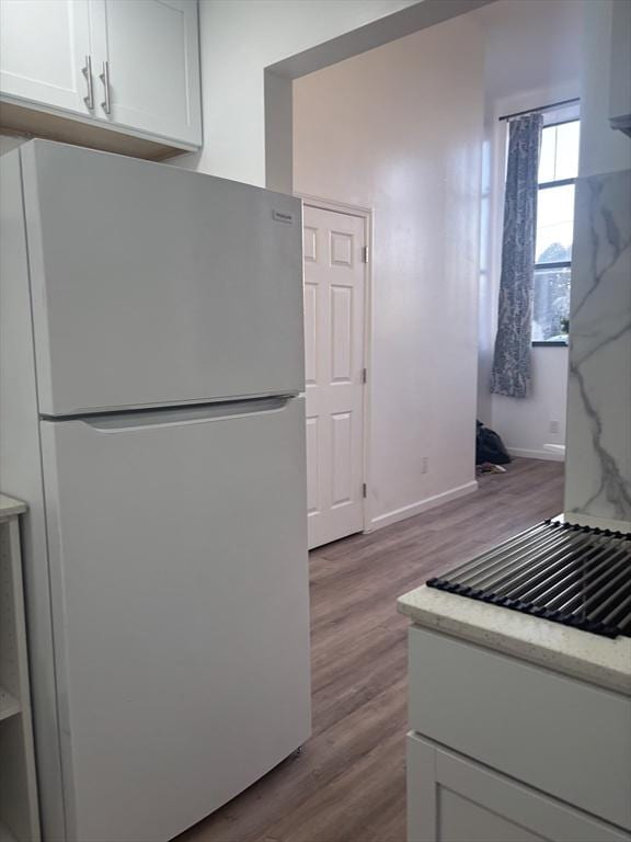 kitchen featuring wood finished floors, freestanding refrigerator, white cabinetry, light stone countertops, and baseboards