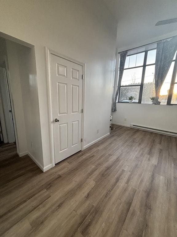 interior space featuring a baseboard heating unit, baseboards, and wood finished floors