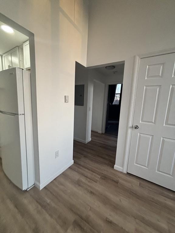 corridor featuring a high ceiling, wood finished floors, electric panel, and baseboards