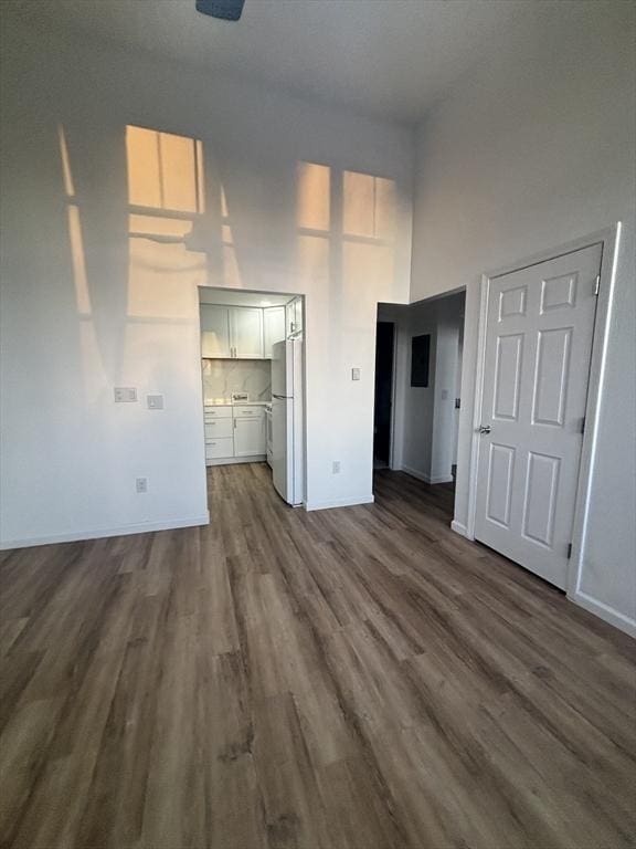 unfurnished bedroom with dark wood-type flooring, a towering ceiling, freestanding refrigerator, and baseboards