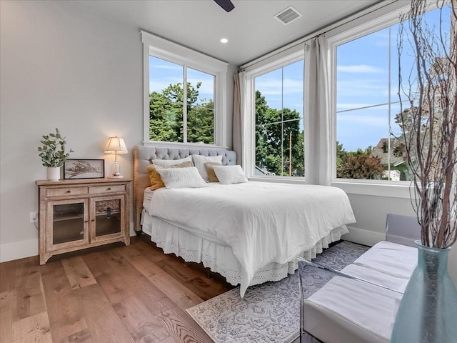 bedroom featuring baseboards, multiple windows, visible vents, and wood finished floors