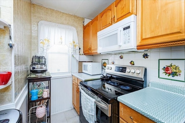 kitchen featuring electric stove, white microwave, light countertops, and tile walls