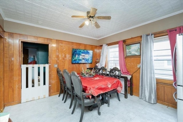 dining room with ornamental molding, wood walls, and ceiling fan