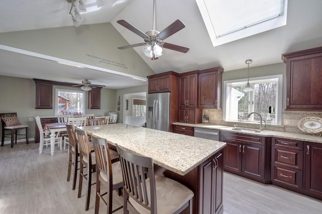 kitchen with a sink, high vaulted ceiling, stainless steel appliances, a ceiling fan, and a kitchen bar