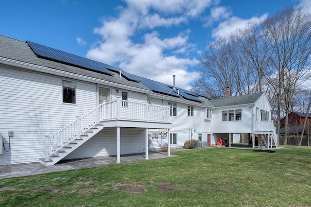 rear view of property with roof mounted solar panels, a yard, and stairway