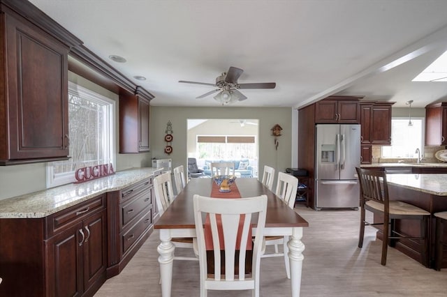 kitchen with stainless steel refrigerator with ice dispenser, ceiling fan, light stone counters, and a wealth of natural light
