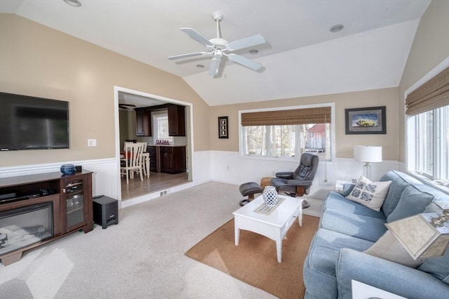 living room featuring a ceiling fan, light carpet, wainscoting, and lofted ceiling