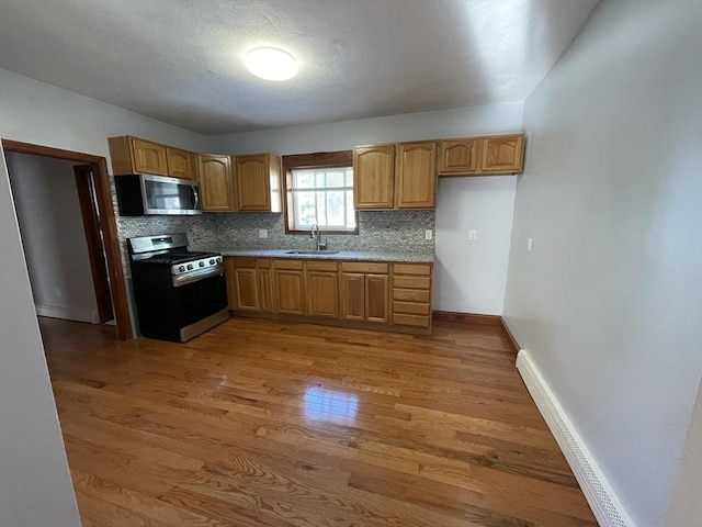 kitchen with a baseboard radiator, sink, decorative backsplash, stainless steel appliances, and light wood-type flooring