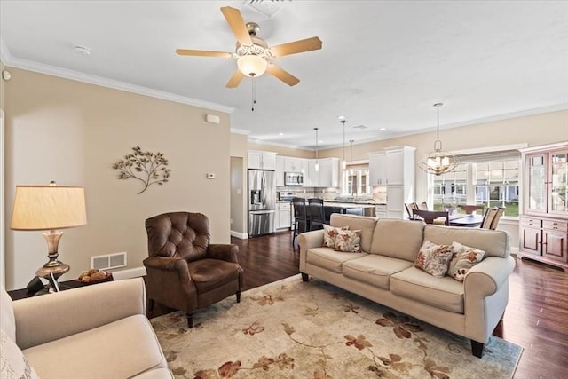 living room with dark hardwood / wood-style flooring, crown molding, and ceiling fan with notable chandelier