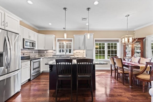 kitchen featuring a kitchen island, decorative light fixtures, white cabinetry, stainless steel appliances, and light stone countertops