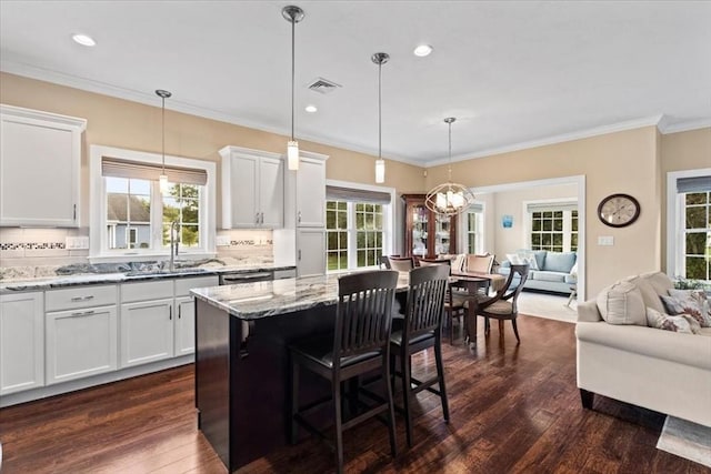 kitchen with a kitchen bar, sink, white cabinetry, decorative light fixtures, and light stone countertops