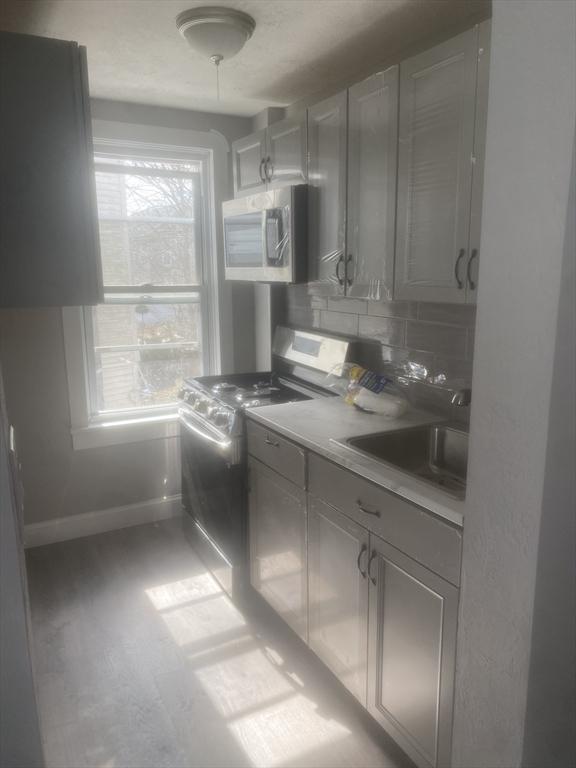 583 Center St, Fall River, MA 02720 - kitchen featuring stainless steel microwave, stove, baseboards, a sink, and decorative backsplash