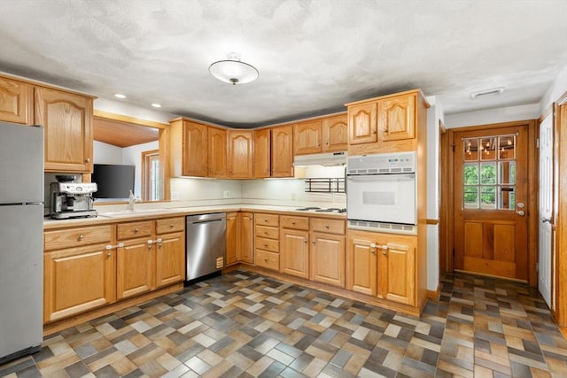 kitchen featuring appliances with stainless steel finishes, light countertops, a sink, under cabinet range hood, and recessed lighting