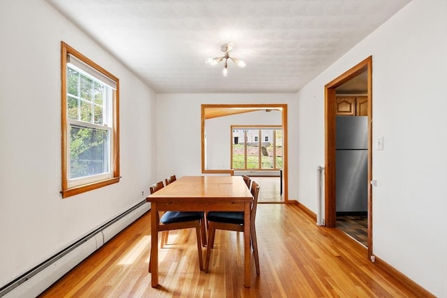 dining area with a baseboard heating unit, light wood-style flooring, a chandelier, and baseboards