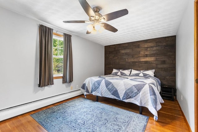 bedroom featuring a baseboard heating unit, wood finished floors, and ceiling fan