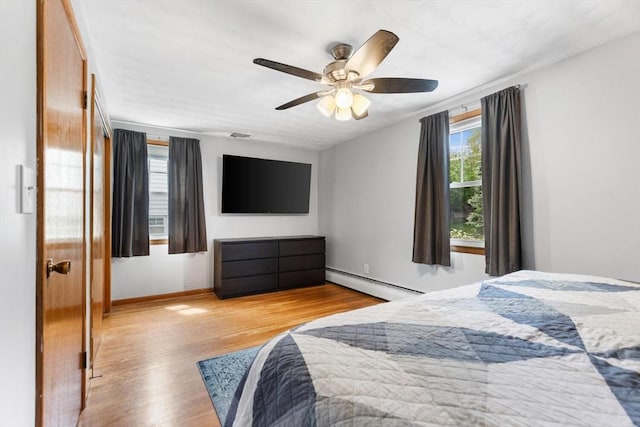 bedroom with baseboard heating, wood finished floors, ceiling fan, and baseboards