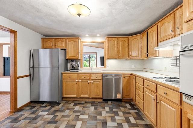 kitchen with stainless steel appliances, light countertops, a sink, under cabinet range hood, and baseboards