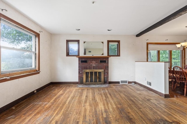 unfurnished living room featuring hardwood / wood-style flooring, beam ceiling, a brick fireplace, and a notable chandelier