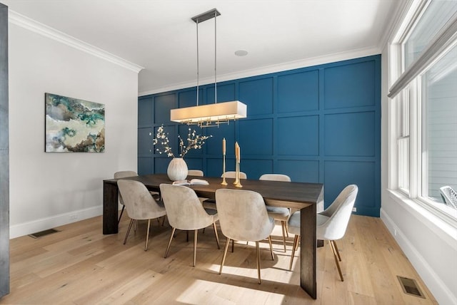 dining area featuring light wood-style floors, visible vents, a decorative wall, and ornamental molding