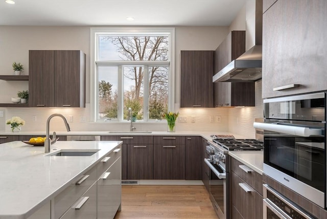 kitchen featuring a sink, wall chimney range hood, appliances with stainless steel finishes, open shelves, and modern cabinets