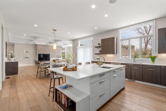 kitchen featuring open shelves, light countertops, a kitchen island with sink, a sink, and modern cabinets