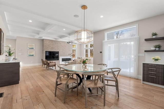 dining space featuring coffered ceiling, a fireplace, baseboards, light wood-type flooring, and beamed ceiling