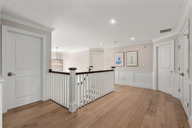 hallway featuring visible vents, crown molding, light wood-style floors, a decorative wall, and a notable chandelier