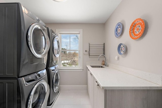 washroom featuring light tile patterned floors, cabinet space, a sink, stacked washing maching and dryer, and baseboards