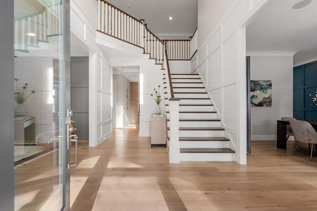 entrance foyer featuring stairs, a high ceiling, light wood-style flooring, and crown molding