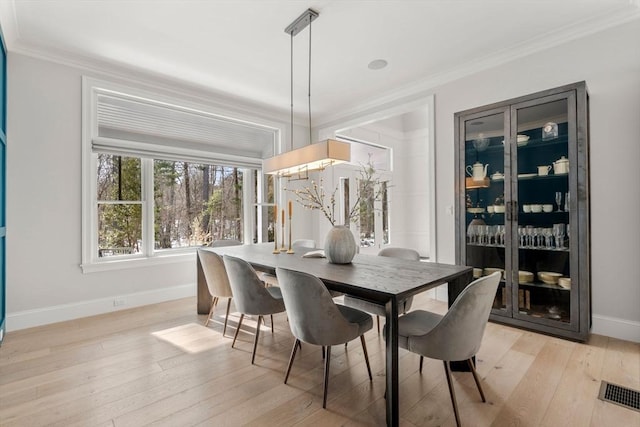 dining area with light wood finished floors, baseboards, visible vents, and crown molding