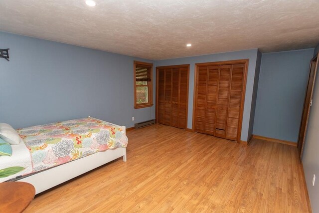 bedroom with cooling unit, a baseboard heating unit, light hardwood / wood-style flooring, and multiple windows