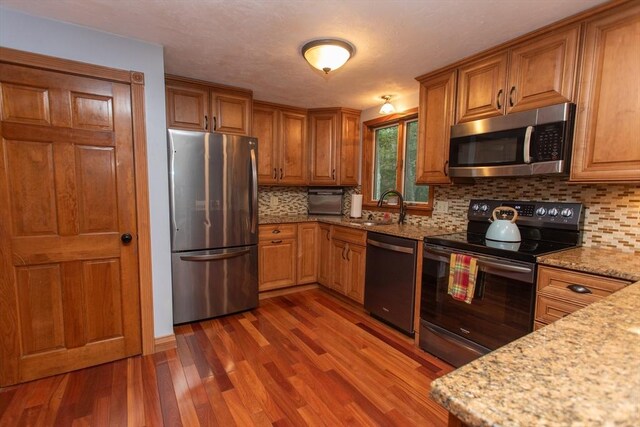 kitchen with backsplash, dark hardwood / wood-style flooring, stainless steel appliances, light stone countertops, and sink