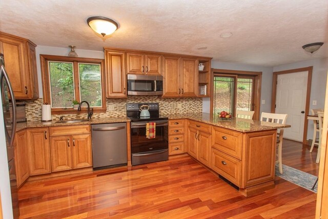 kitchen with appliances with stainless steel finishes, sink, light stone counters, decorative backsplash, and light wood-type flooring