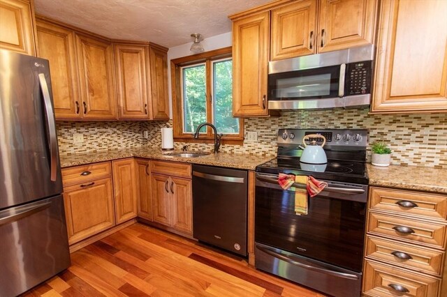 kitchen with backsplash, light stone counters, stainless steel appliances, and light hardwood / wood-style floors