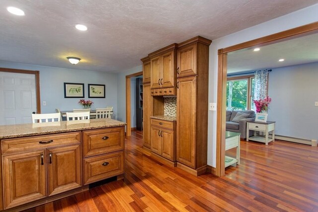 kitchen with a baseboard radiator, decorative backsplash, light stone counters, and dark wood-type flooring