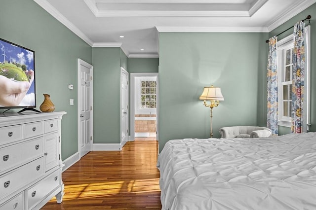 bedroom with ornamental molding, ensuite bathroom, hardwood / wood-style floors, and a raised ceiling