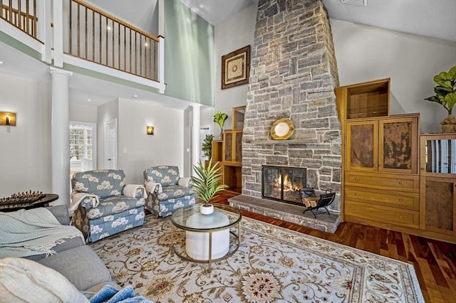 living room with a towering ceiling, a stone fireplace, decorative columns, and hardwood / wood-style floors