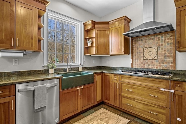 kitchen featuring wall chimney range hood, stainless steel appliances, sink, and dark stone counters