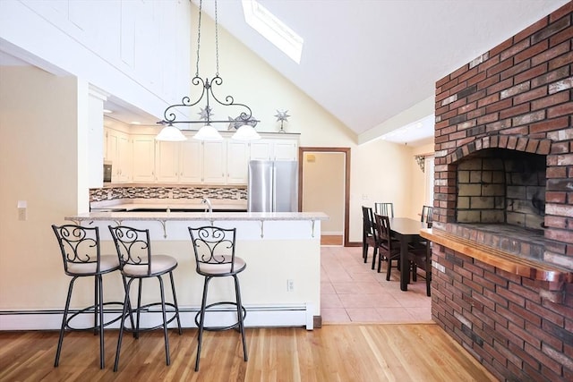 kitchen with pendant lighting, a skylight, stainless steel fridge, light hardwood / wood-style floors, and kitchen peninsula