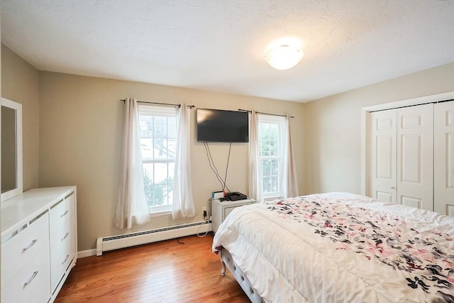 bedroom featuring light wood-type flooring, a closet, multiple windows, and a baseboard heating unit