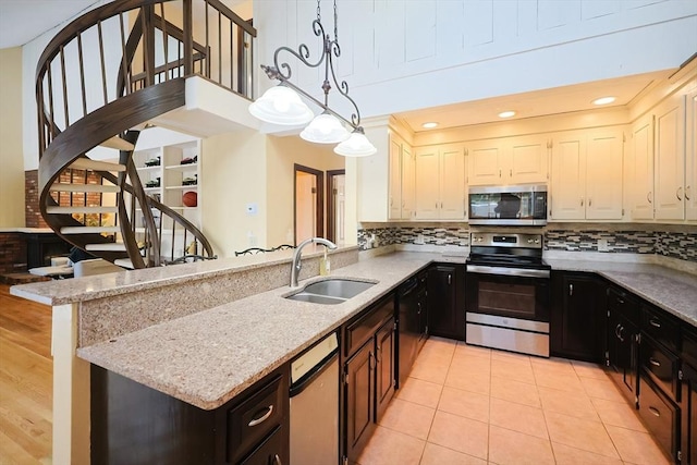 kitchen with appliances with stainless steel finishes, backsplash, light stone counters, sink, and decorative light fixtures