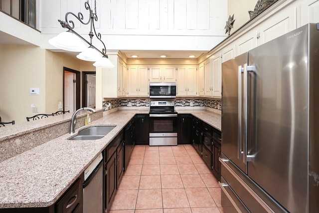 kitchen featuring decorative backsplash, appliances with stainless steel finishes, light stone counters, sink, and hanging light fixtures