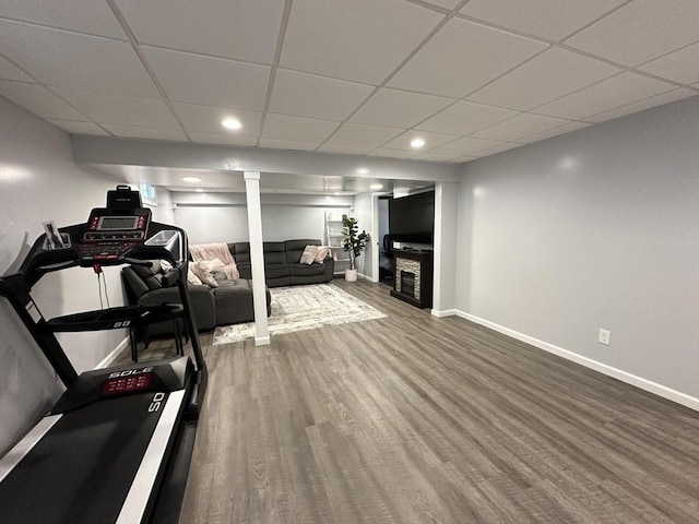 exercise room featuring a drop ceiling, hardwood / wood-style flooring, and a stone fireplace