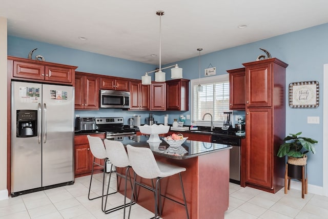 kitchen with a kitchen island, appliances with stainless steel finishes, a kitchen bar, hanging light fixtures, and sink